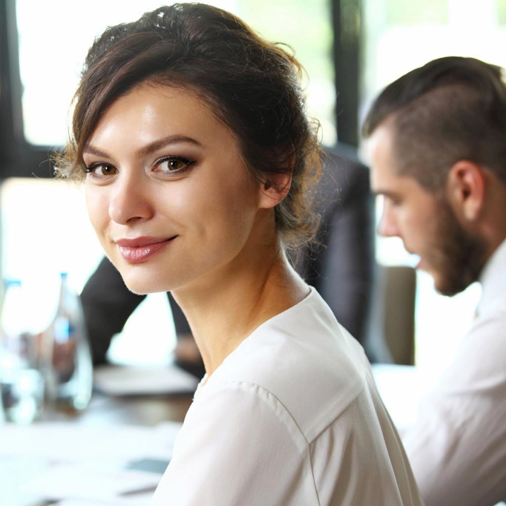 A man and a woman in an office, woman looking at the photographer